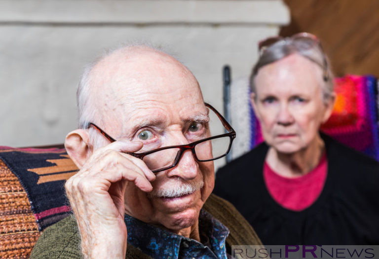 Concerned elderly couple sitting in livingroom scowling