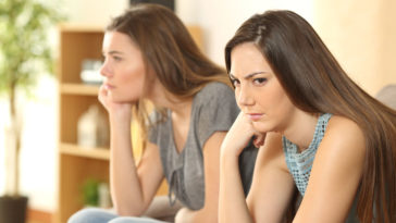 Angry friends or roommates sitting on a sofa in the living room at home, hostile roommate